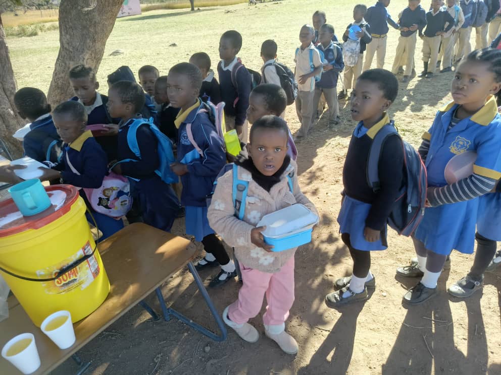 A vibrant community scene in Eswatini with children reading books under a tree, women receiving vocational training, and a small community garden with fresh vegetables in the background